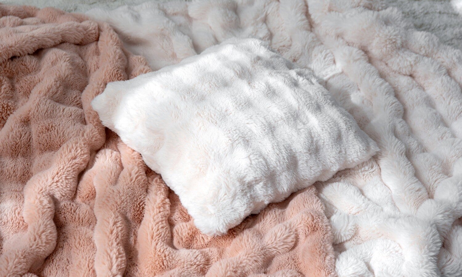Soft throws and a fluffy cushion in light tones, styled as inspiration for a cosy and inviting home.
