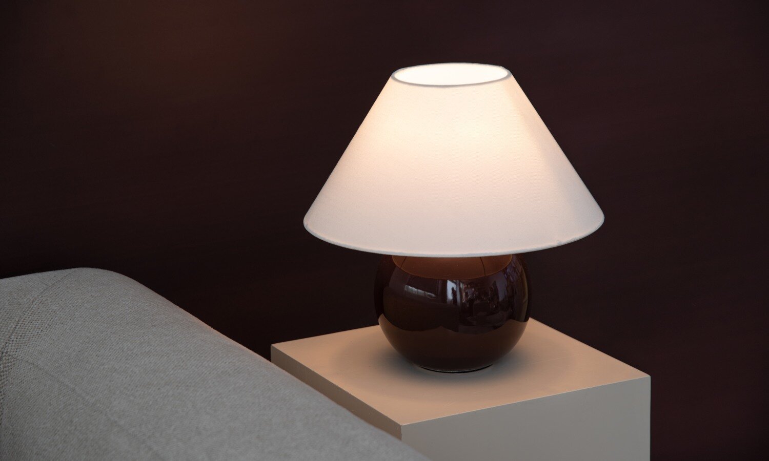 Lit table lamp with a white lampshade and a dark brown rounded base on a side table.