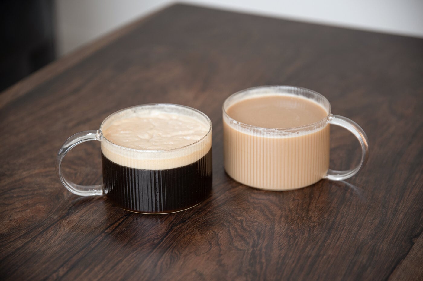 Two mugs in glass with coffee on a brown wooden table.