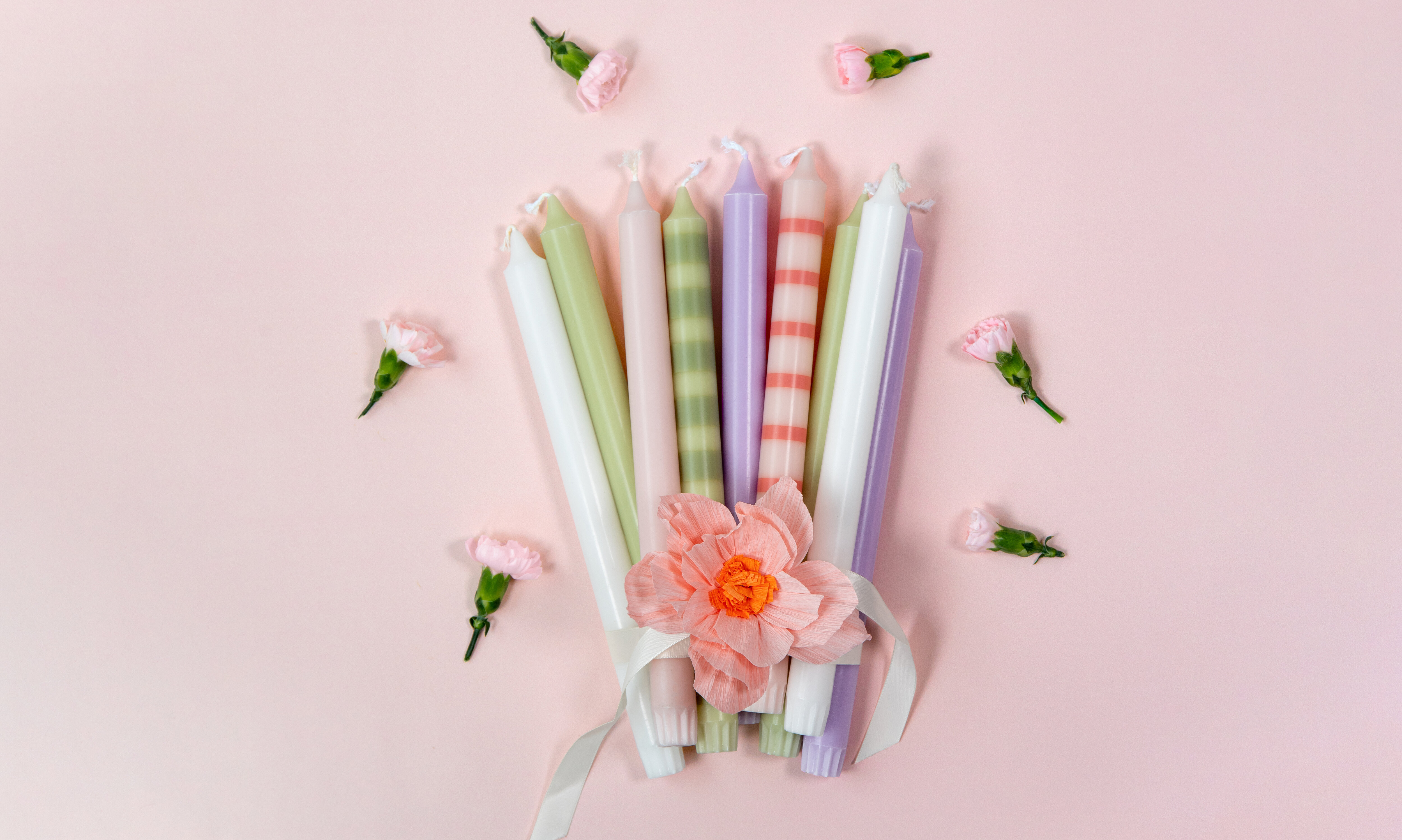 Pastel-colored candles with striped details and a decorative flower on a pink background.